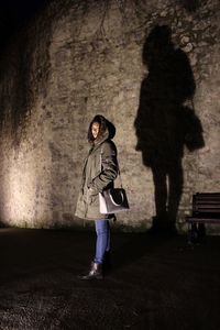 Portrait of woman standing against wall at night