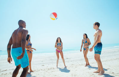 Friends playing with ball at beach against sky