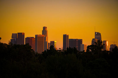Trees and buildings against clear sky during sunset
