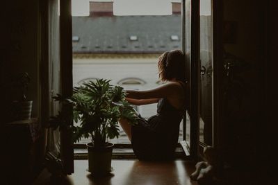 Side view of woman standing by potted plant at home