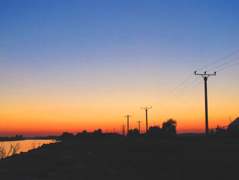 Silhouette electricity pylon against clear sky during sunset