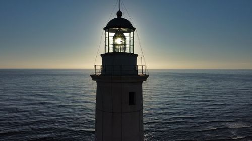 Lighthouse by sea against sky during sunset