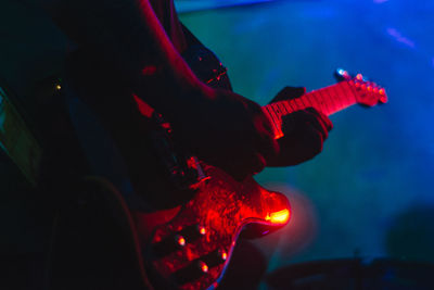 Midsection of man playing illuminated guitar at night