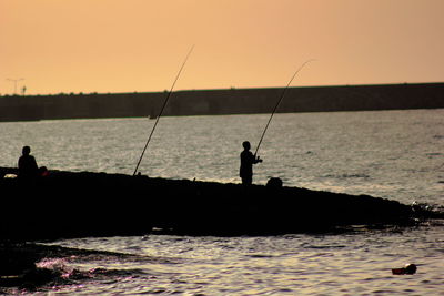 Silhouette man fishing in sea against clear sky