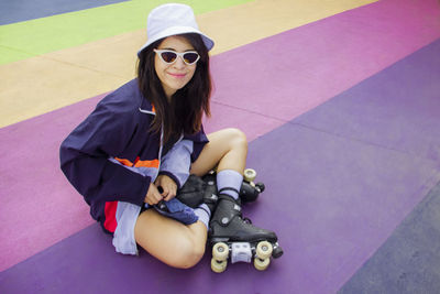 Smiling woman wearing roller skates sitting on multi colored floor