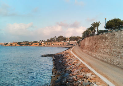 Road by sea against sky during sunset