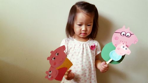 Cute girl holding toys while standing against wall