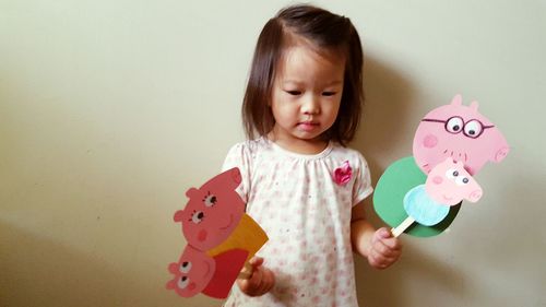 Cute girl holding pink toy against wall