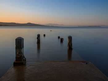 Wooden posts in sea against sky at sunset