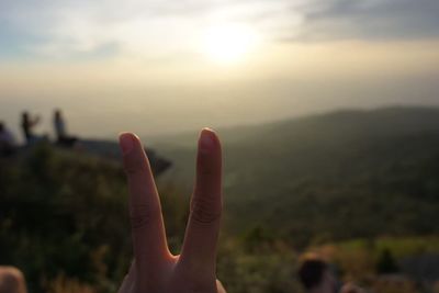 Close-up of hand against sky during sunset