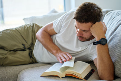 Young woman reading book while lying on bed at home