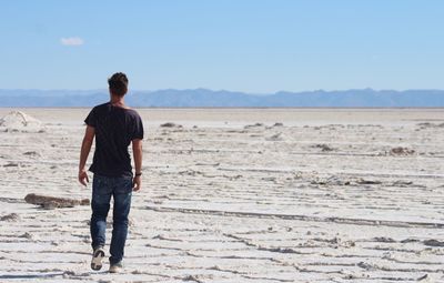 Rear view of man walking on sand at desert against sky