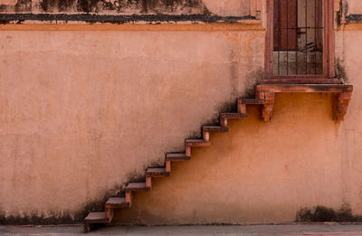Traditional staircase leading to a metal closed door outside an orange wall of an indian house