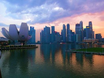 Modern buildings by river against sky during sunset