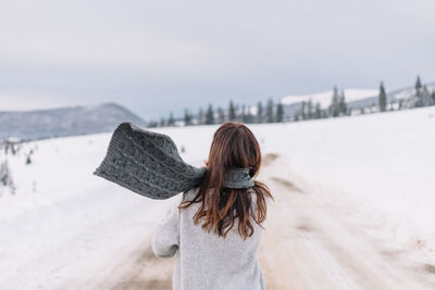 Woman walking on a road cover with snow while on a road trip in the mountains.