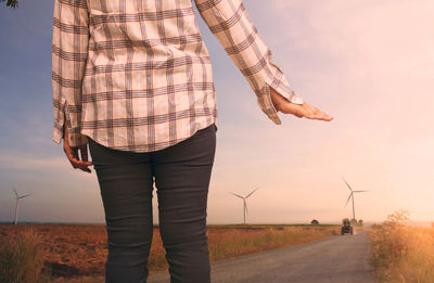 Midsection of woman hailing on road by field against sky