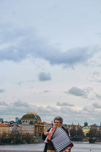 Man standing by building against cloudy sky