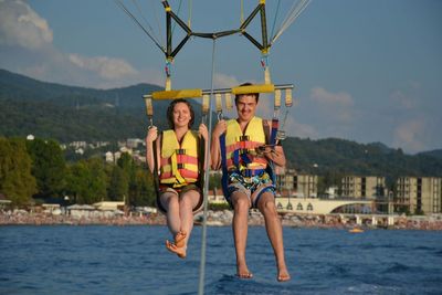 Full length portrait of smiling couple parasailing over river