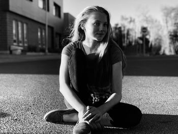 Full length of young woman looking away while sitting on road in city