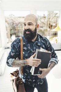 Male architect looking away while holding books at home