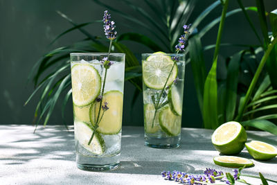 Cool lavender lemonade with lime slices and lavender flower on the table near dark green surface