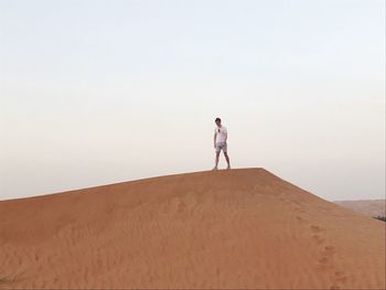 Low angle view of man walking at desert against clear sky during sunset