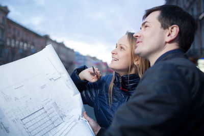 Smiling engineers holding blueprint while standing in city