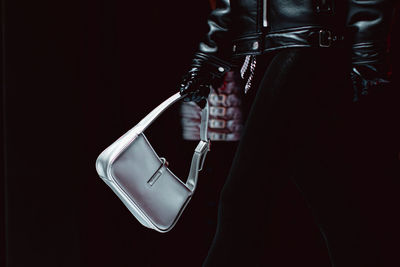 A female hand in a black leather glove holding a classic leather silver handbag