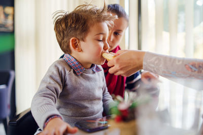 Mother feeding food to son while sitting with friend at restaurant