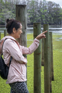 Side view of woman standing by fence against plants