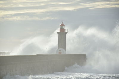 Lighthouse by sea against sky with the big wave