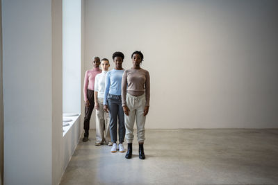 Female friends standing in row against wall at home