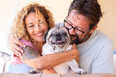 Smiling mature couple embracing pug at table