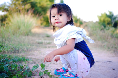 Portrait of girl crouching by plants on land