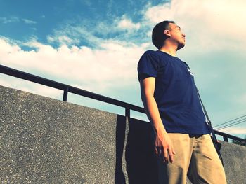 Low angle view of young man looking away against sky