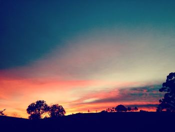 Silhouette trees against dramatic sky during sunset