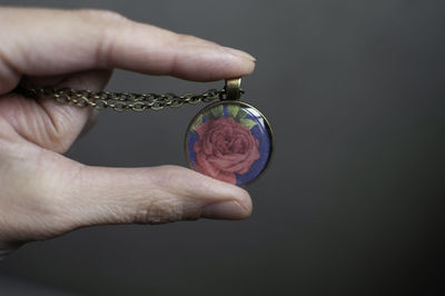 Close-up of hand holding pendant against gray background