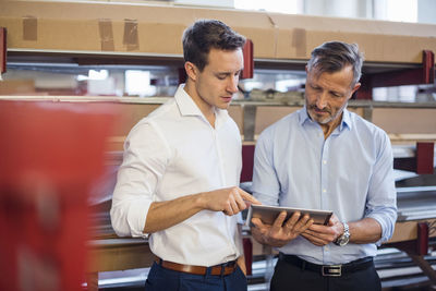 Two businessmen in factory storeroom looking at tablet