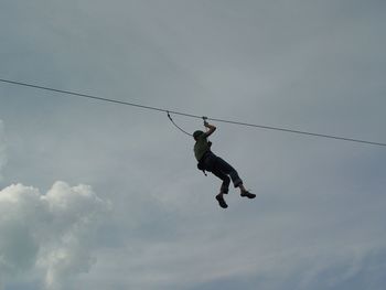 Low angle view of man hanging on rope against sky