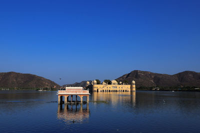 Built structure by lake against clear blue sky