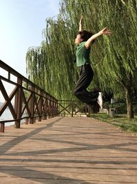 Side view of woman jumping by railing against trees