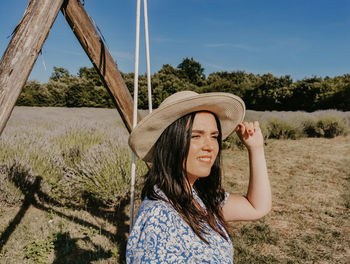 Beautiful young woman sitting on wooden swing in lavender field