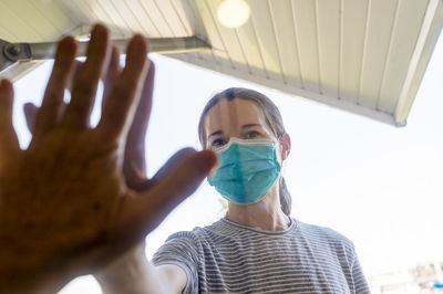 Portrait of woman wearing flu mask touching mirror outdoors