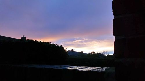 Silhouette buildings by sea against sky during sunset