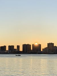 Sea by buildings against clear sky during sunset