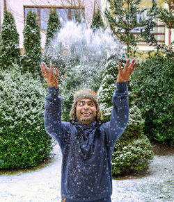 Cheerful man enjoying winter snowfall by throwing snow in the air with hands in snowy garden