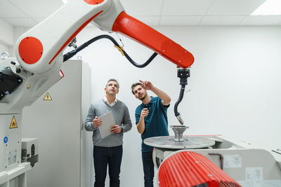 Young male engineer pointing at machinery while discussing with mature entrepreneur in factory