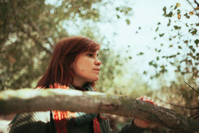 Portrait of young woman looking away against trees