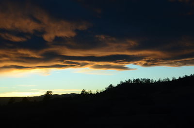 Silhouette landscape against dramatic sky during sunset