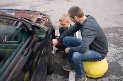 Cute boy helps dad fix the car. unscrew the wheel